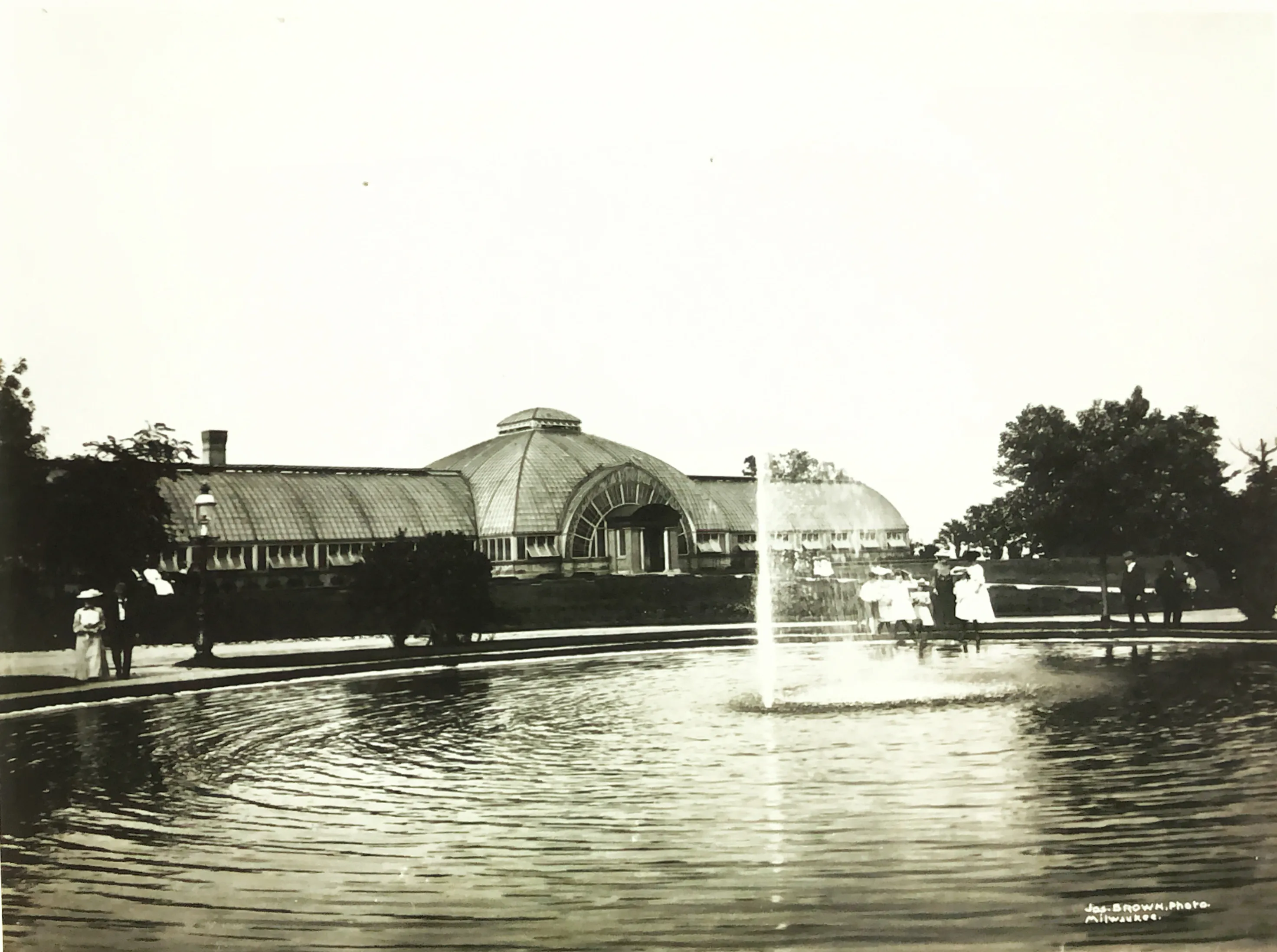 men and women in formal attire view a fountain outside of the conservatory in the early 20th century